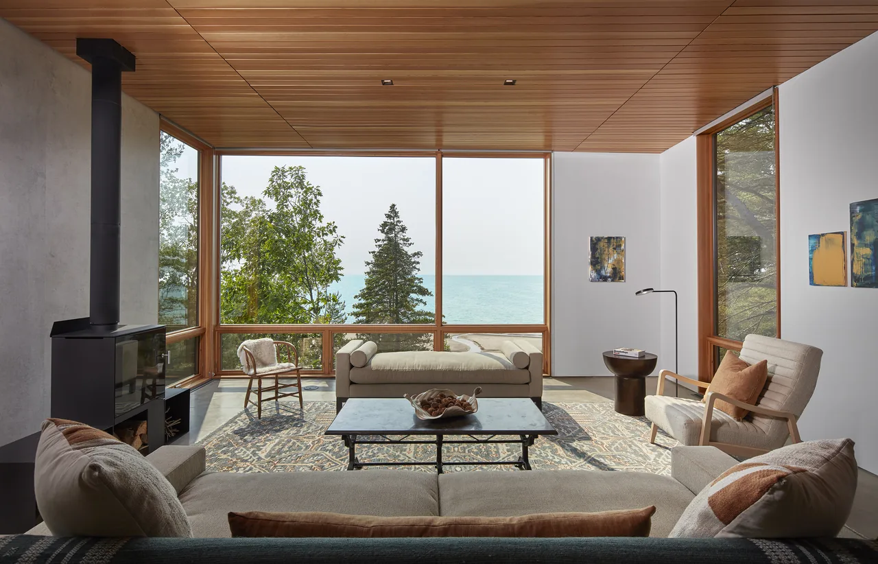 Living room with large floor-to-ceiling wood-framed windows and a freestanding wood stove.