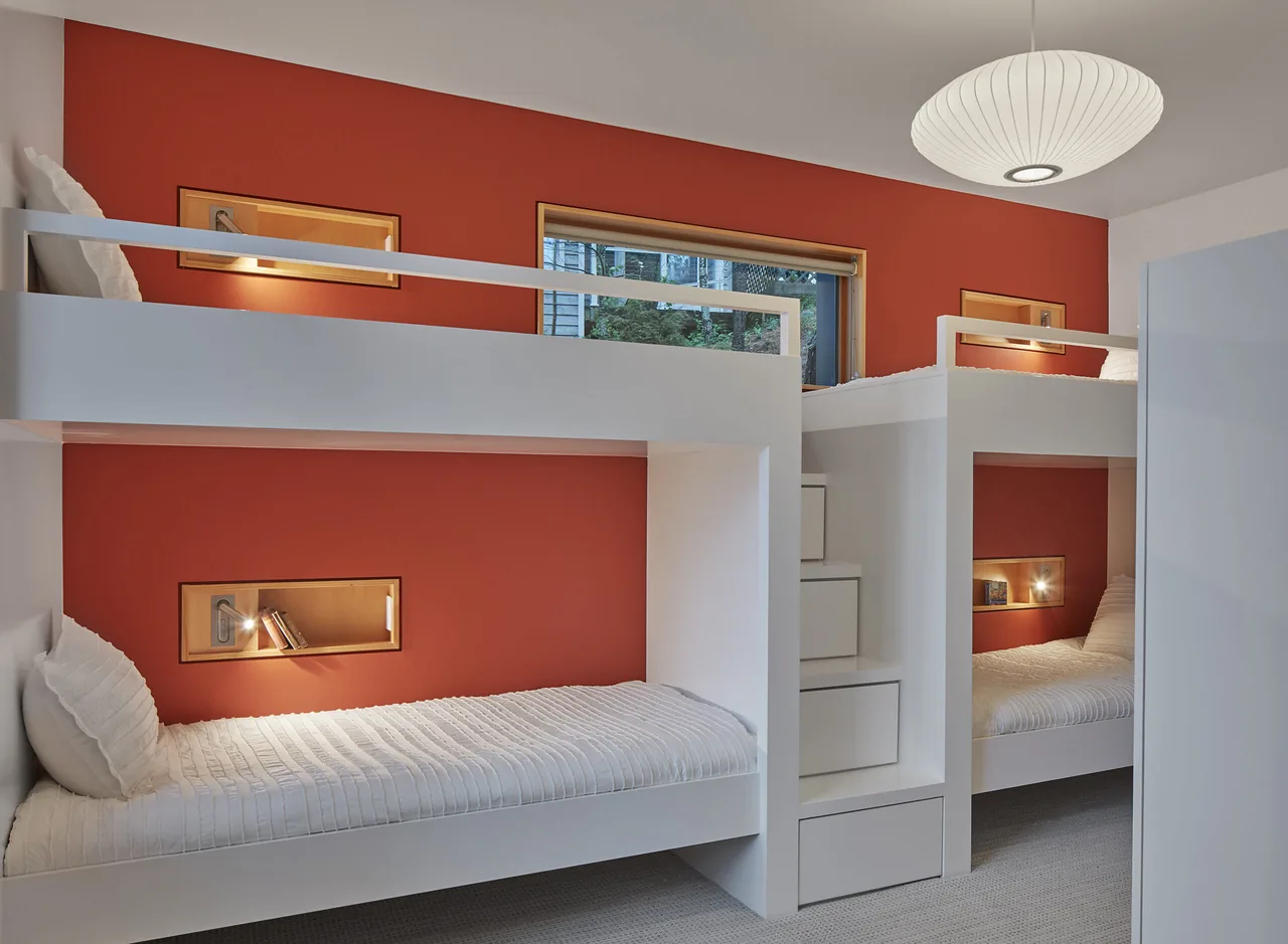 Bedroom featuring two white bunk beds with built-in reading nooks and a red-orange accent wall.