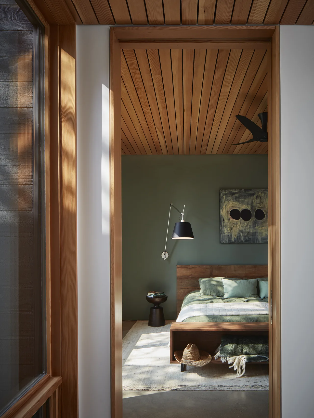 Bedroom interior with wood slat ceiling, green painted wall, and modern wall-mounted reading lamp.