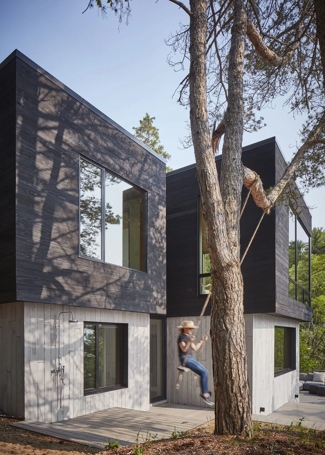 Two-story modern retreat with contrasting black and white wood siding and floor-to-ceiling windows.