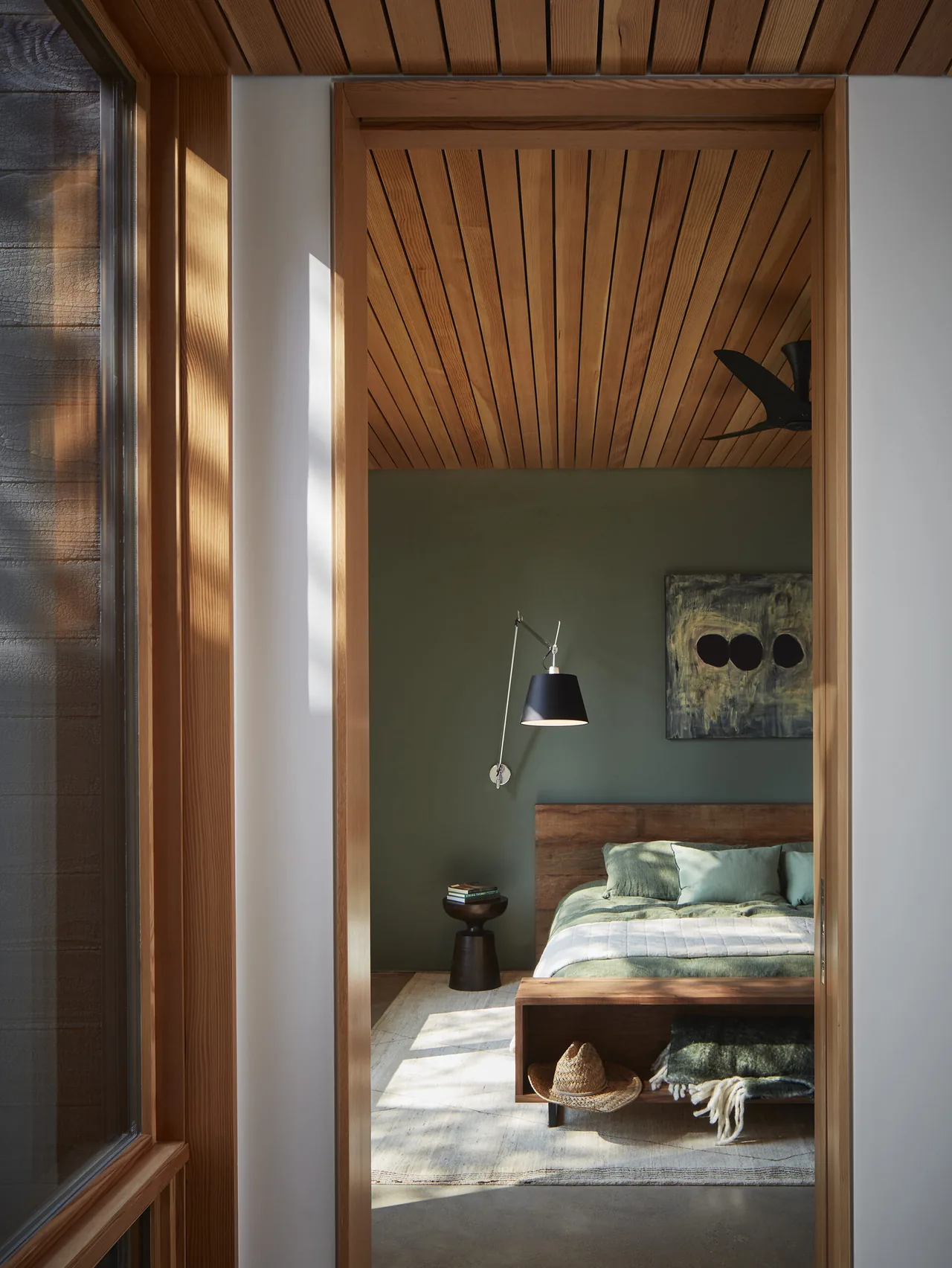 Interior of a bedroom featuring a wood slat ceiling, green walls, and a wooden-framed bed with green bedding.
