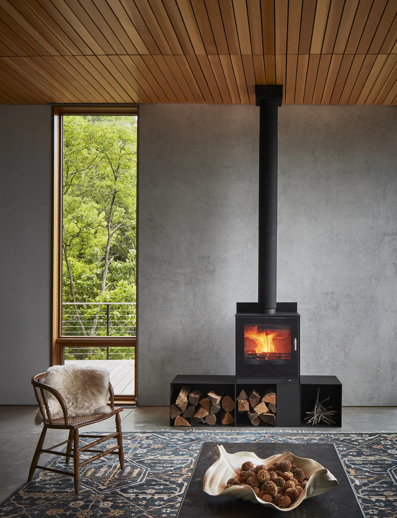 Modern interior with a black wood stove, vertical window, and wood storage below.