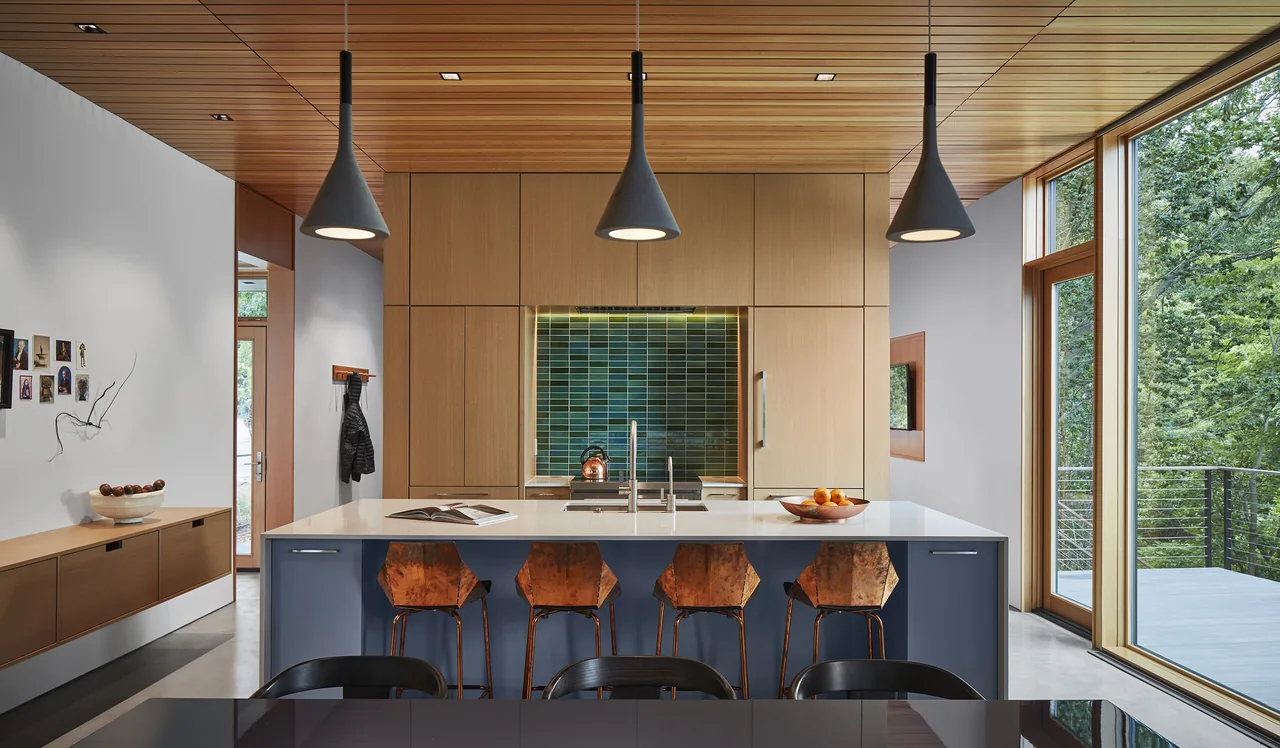 Kitchen with central island, wood cabinetry, and large windows overlooking greenery.
