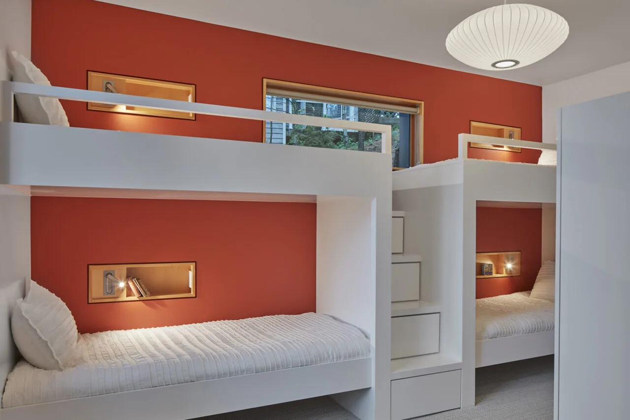 Interior view of a bedroom featuring custom white bunk beds built against a red accent wall with integrated lighting and shelving.
