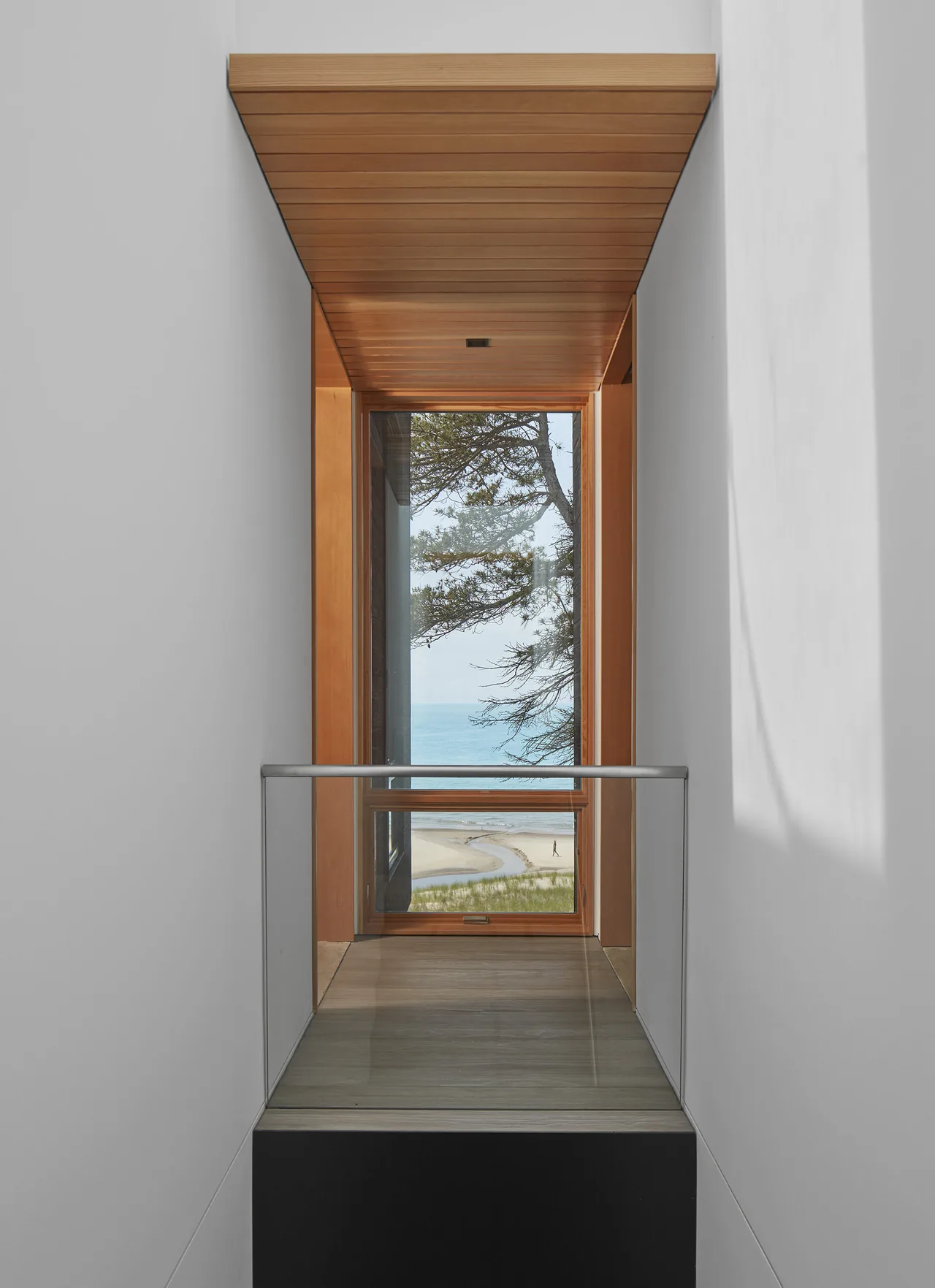 Interior corridor with a wooden ceiling leads to a large framed window overlooking the beach and water.
