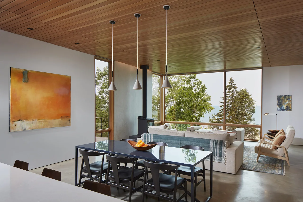 Open living and dining area with floor-to-ceiling glazing and wood ceiling in a modern residence.