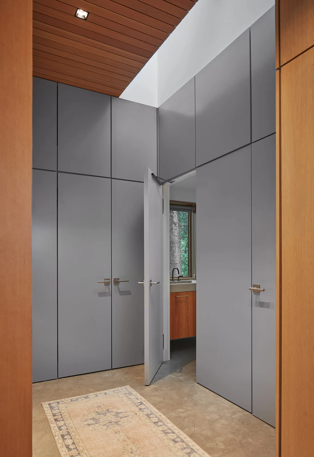 Tall matte gray built-in cabinets with metal handles surround a passage to a bathroom with wooden cabinets visible.