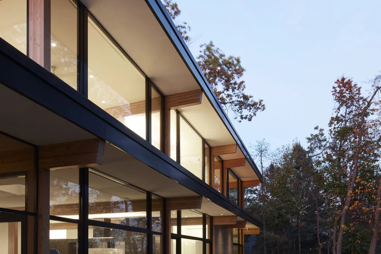 Modern two-story building with extensive glazing, exposed wood beams, and flat roof set in natural surroundings.