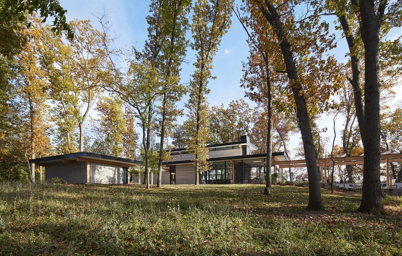 The Galien River Retreat features flat rooflines and extensive glazing among tall trees in an autumn setting.