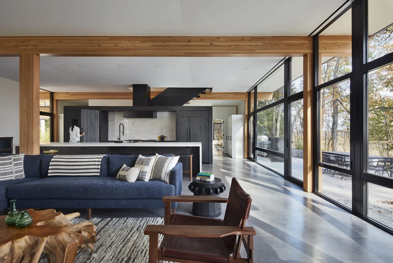 Living room and kitchen area with polished concrete floors and large glass windows overlooking a wooded exterior space.