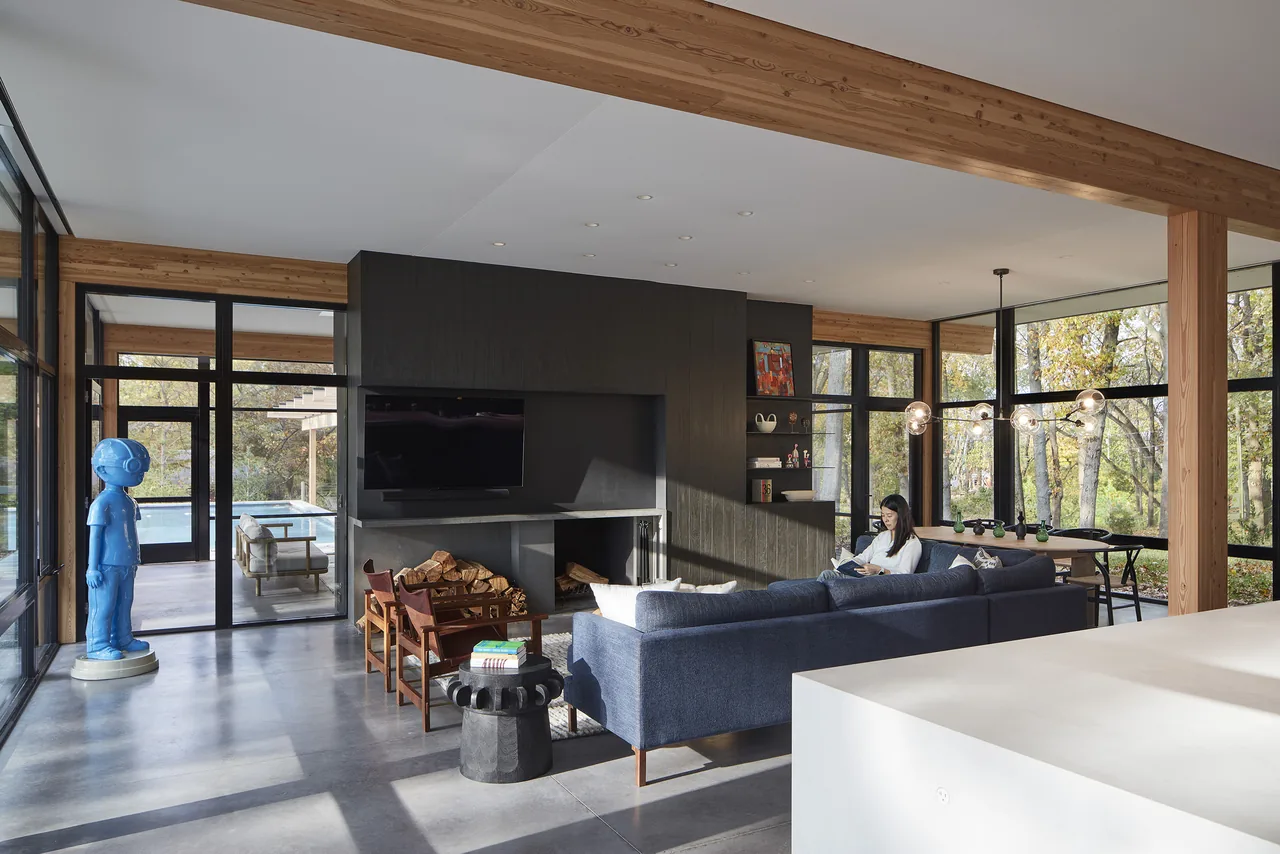 Open plan living room with large windows overlooking wooded surroundings.