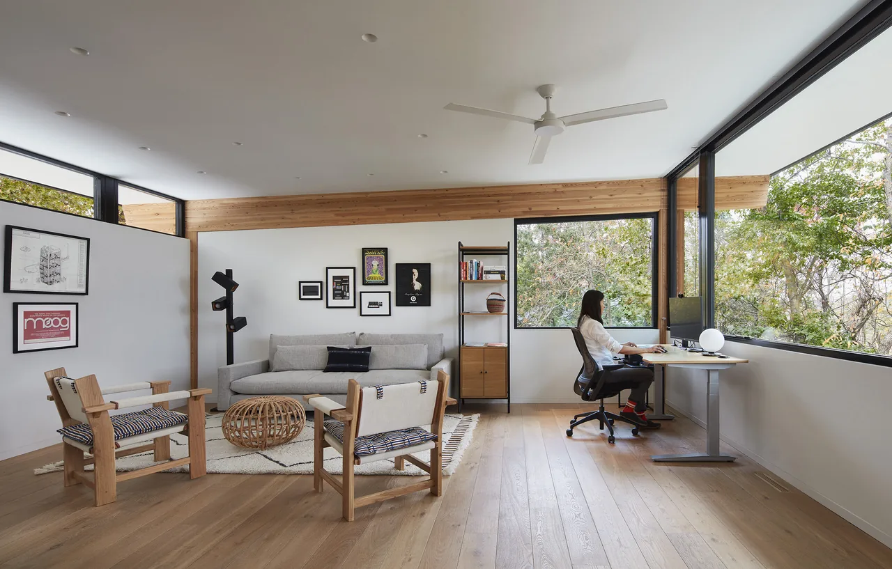 Living room and office area with floor-to-ceiling corner windows and wood flooring.