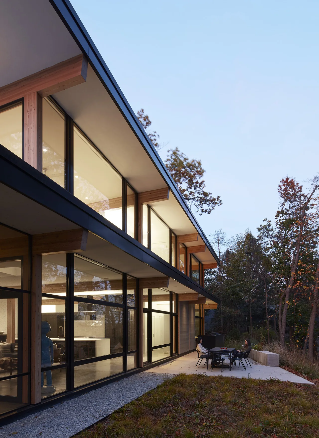 Modern retreat features floor-to-ceiling glazing with exposed wood beams and outdoor seating area.