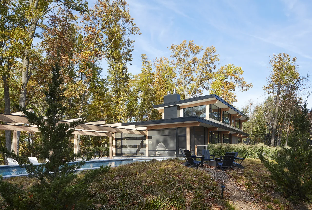 Exterior view of the Galien River Retreat showing the house with extensive glazing and a pool with a wooden pergola.