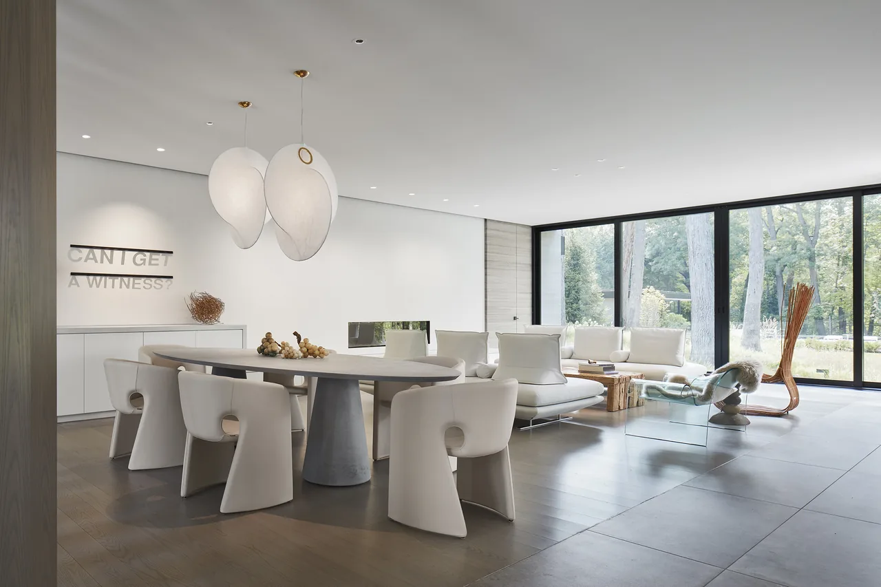 Two Gables project features a combined living and dining space with neutral colors and expansive glazing overlooking greenery.