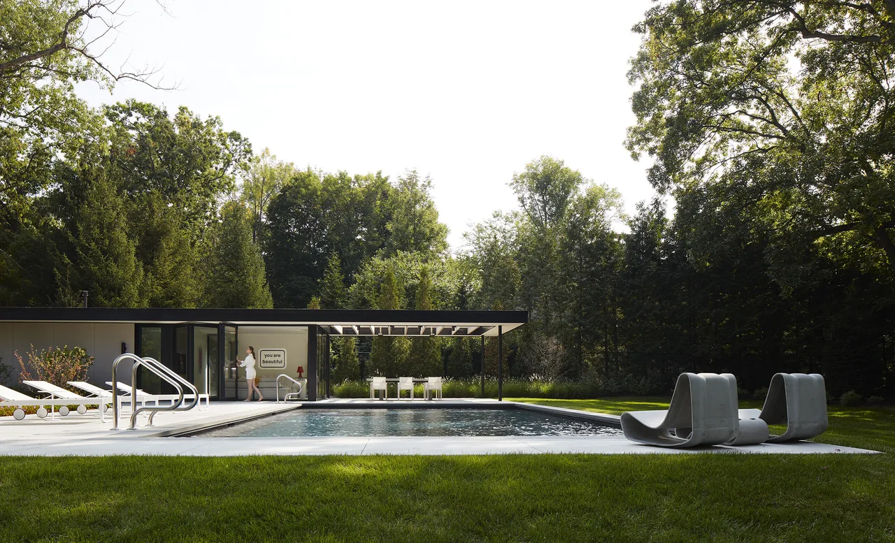 Exterior rear view of a modern house with a covered patio and rectangular pool in a green wooded setting.