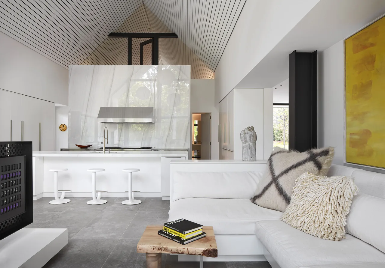 Open living and kitchen space with a vaulted ceiling and a white island featuring seating for three in the Two Gables project.