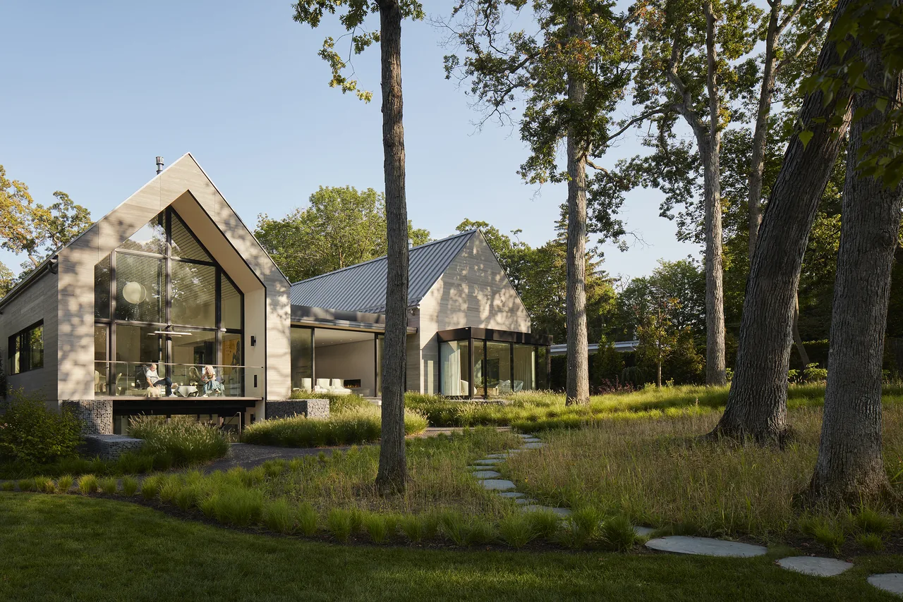 Two-gabled house with a metal roof features large glass windows and lush ornamental grass landscaping.