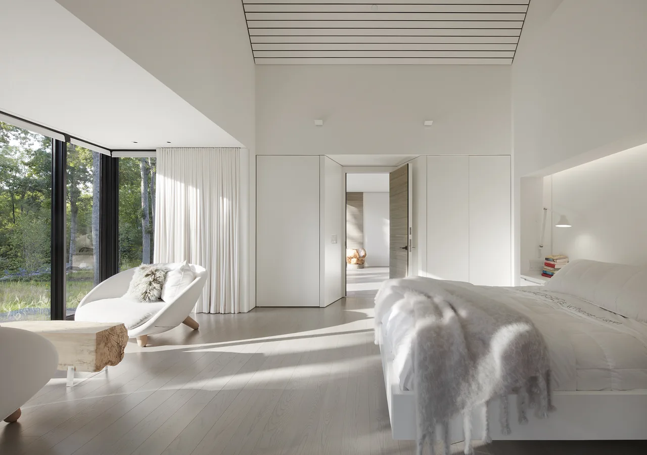 Bedroom featuring floor-to-ceiling corner windows and light wood floors with minimal furnishings.