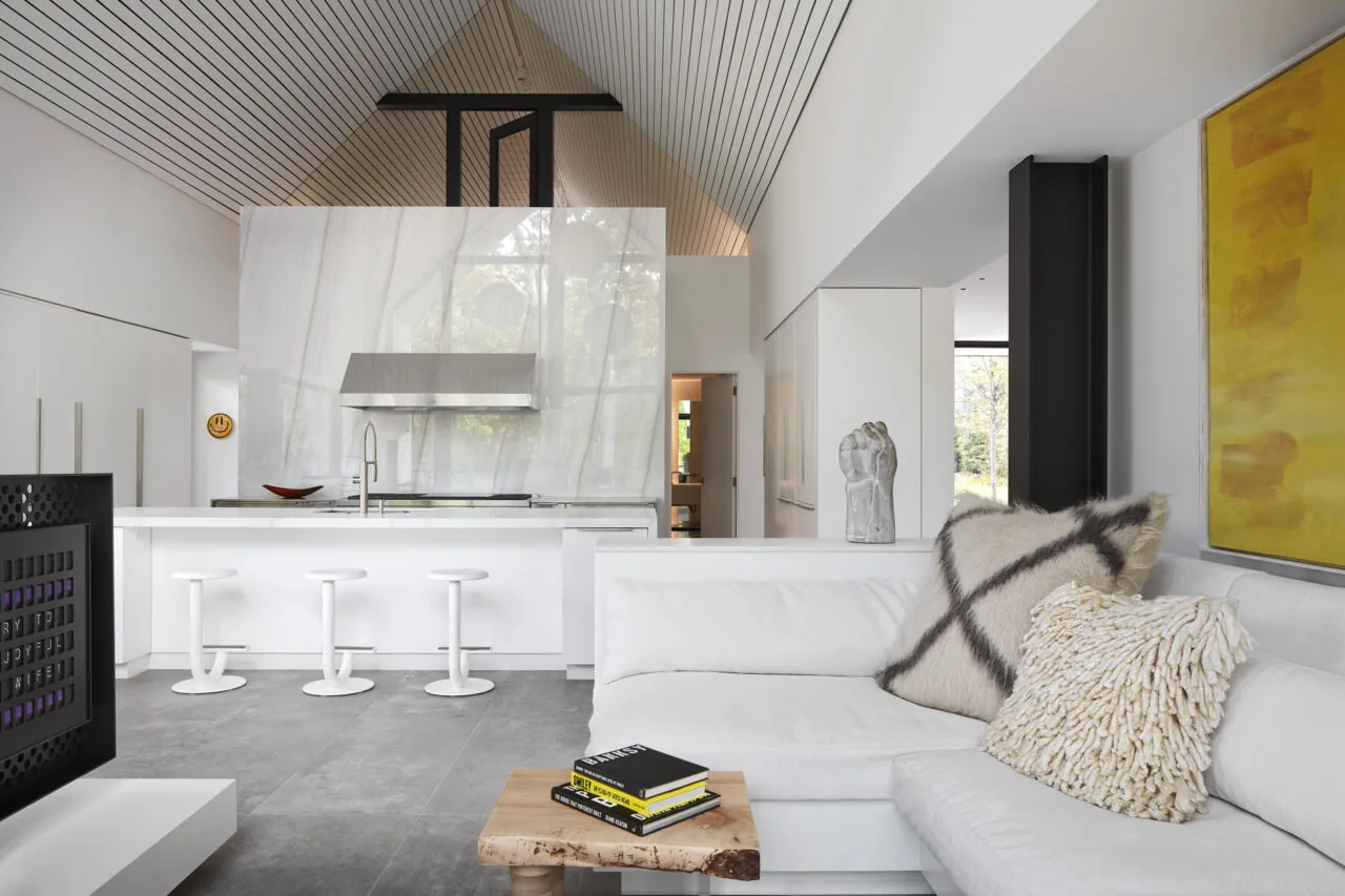 Living room looking toward kitchen with vaulted ceiling and white marble backsplash extending up the wall behind a stainless steel range hood.