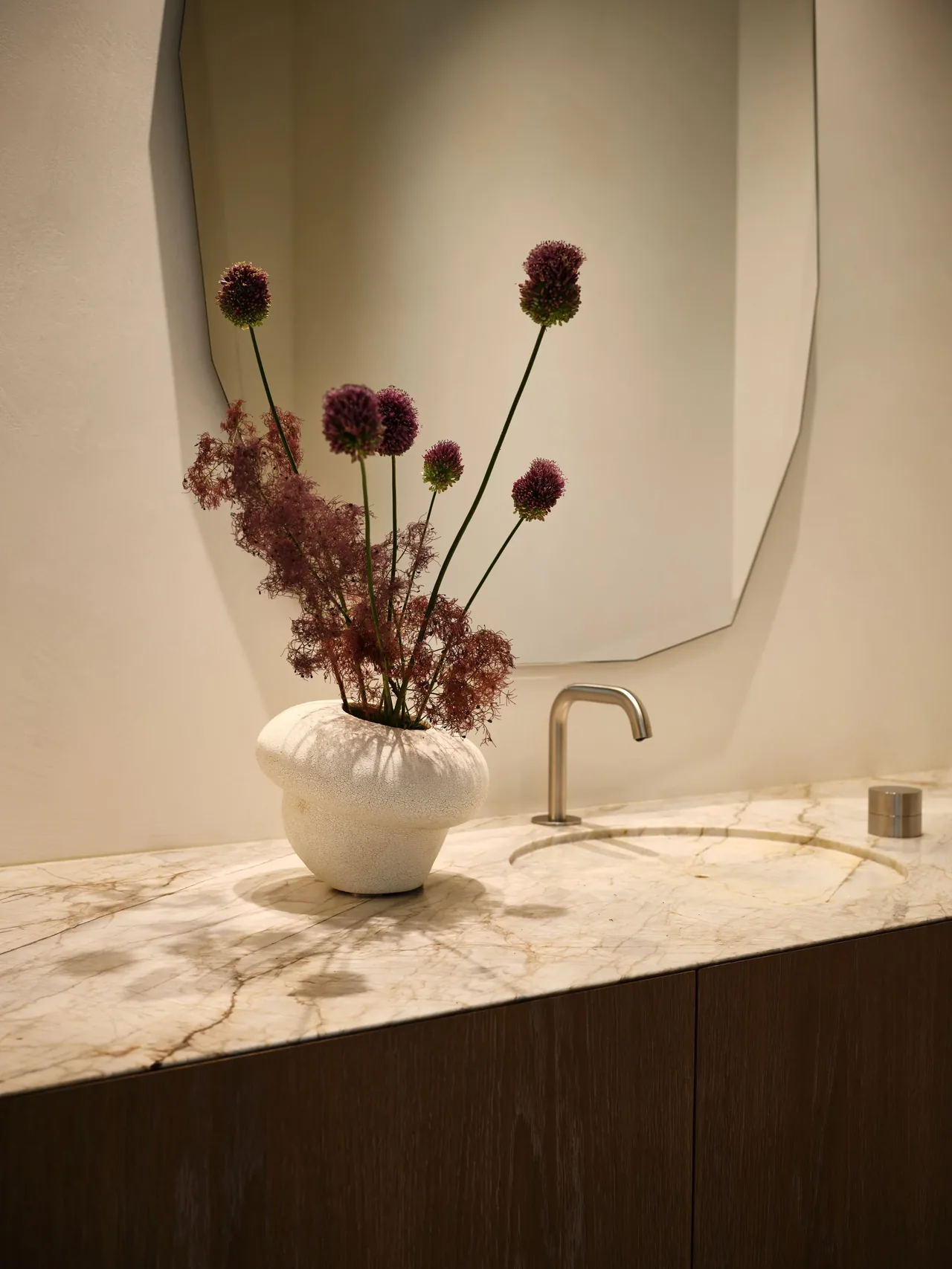 Bathroom vanity with marble countertop, built-in sink, curved faucet, and decorative vase with flowers.