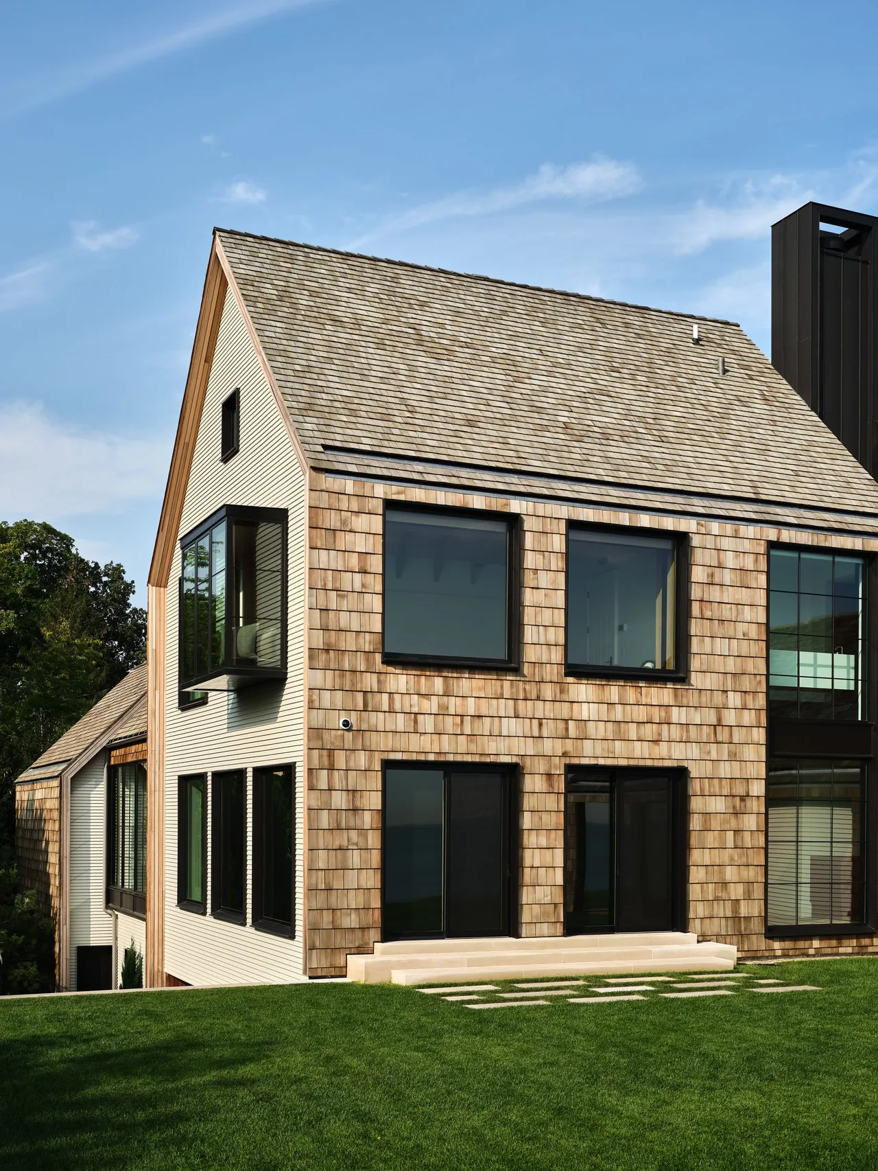 Exterior front view of a modern house featuring wood shingles, a steep pitched roof, and black metal framed windows.