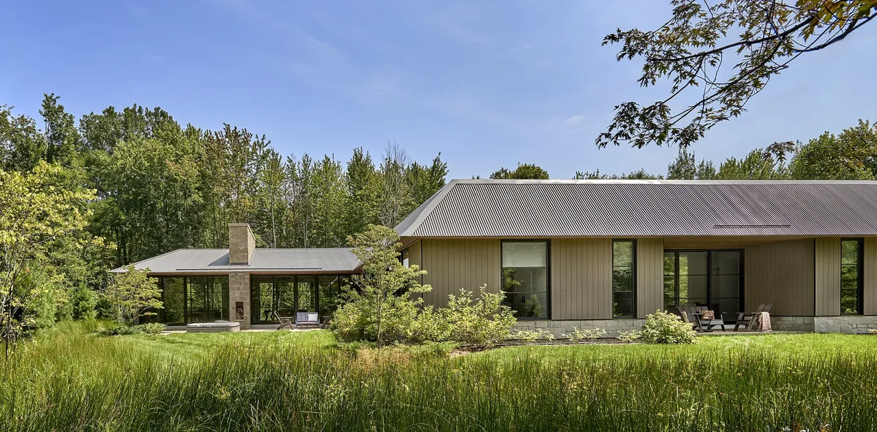 Prairie Road Retreat features a low, single-story structure with vertical siding and a corrugated metal roof amid natural landscaping.