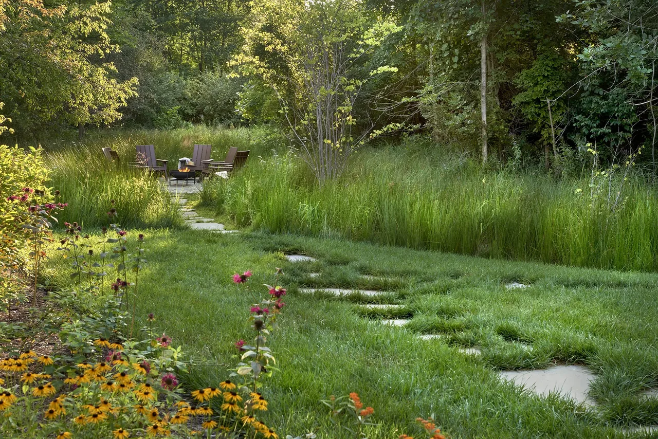 Outdoor seating area with wood chairs and a fire pit surrounded by lush greenery and wildflowers.