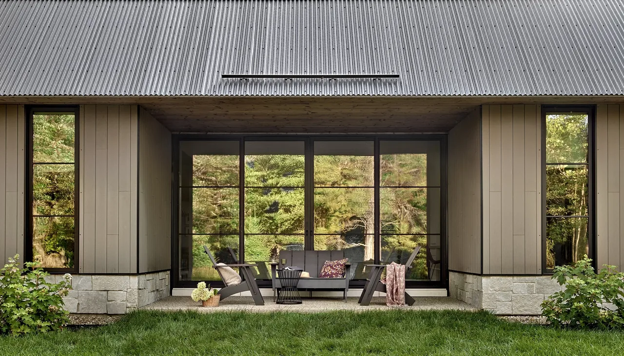 Porch area of Prairie Road Retreat with large black window frames and outdoor furniture under a steel roof.