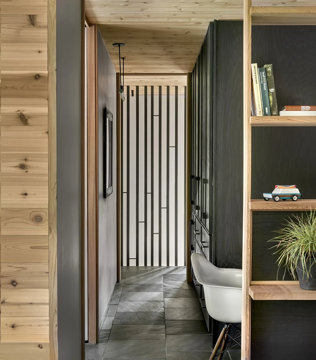 Interior hallway features slate flooring, wood ceiling, black cabinetry, and a vertical wood slat wall.