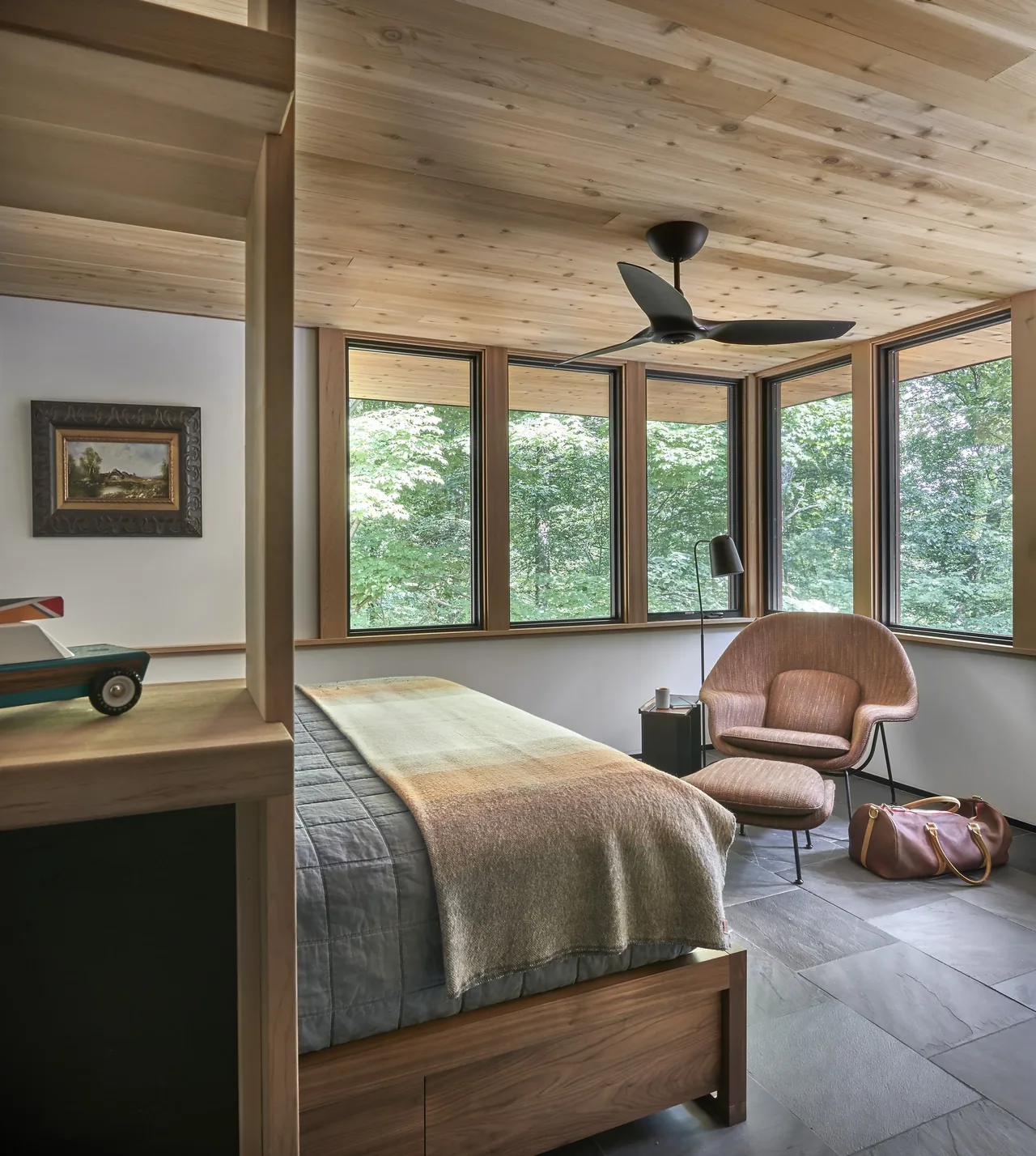 Bedroom featuring wood-paneled ceiling and multiple corner windows looking out to greenery.