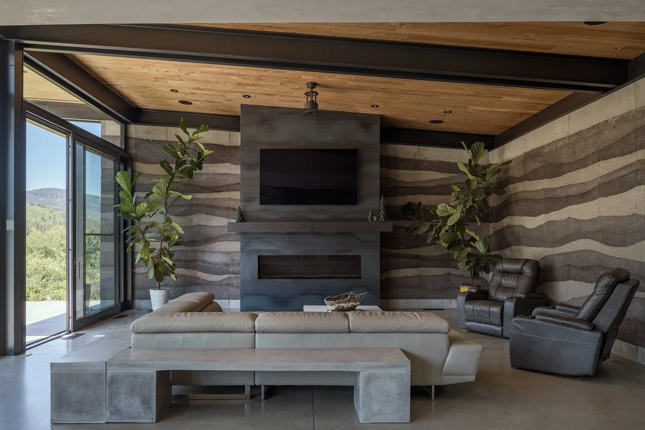 Living room features layered rammed earth walls and a metal-clad fireplace with TV above.