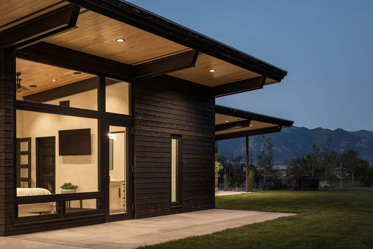 Freedom Residence showing dark horizontal wood siding, extensive glazing, and expansive roof overhangs at dusk.