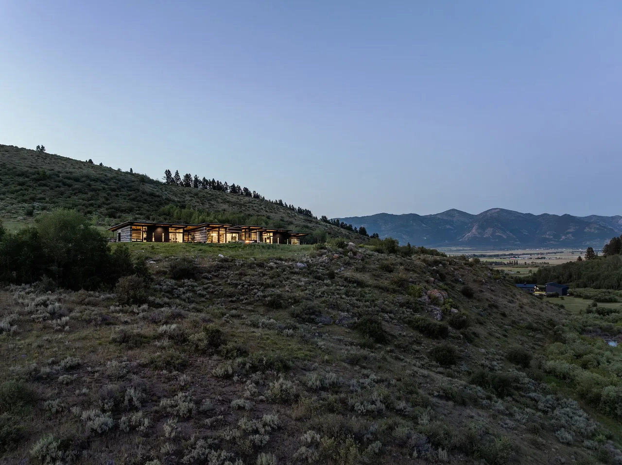 Freedom Residence sits on a hillside overlooking a valley with mountain views during dusk.