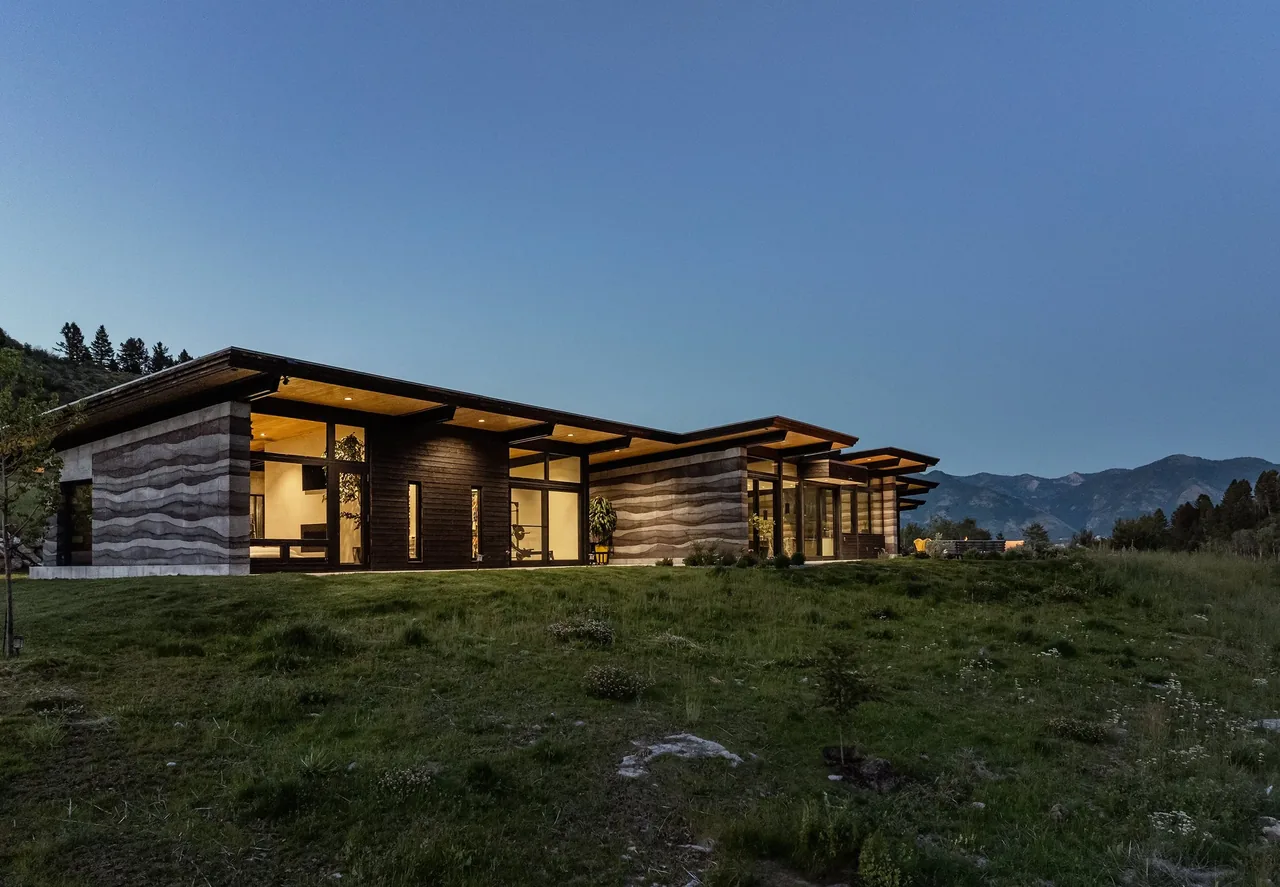 Exterior side view of a low modern residence with layered concrete walls and extensive floor-to-ceiling glazing under a flat roof.