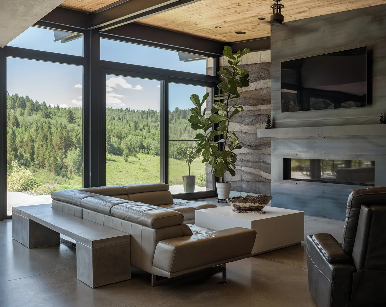 Living room featuring floor-to-ceiling glazing, a concrete bench, and a wall-mounted TV above the fireplace.