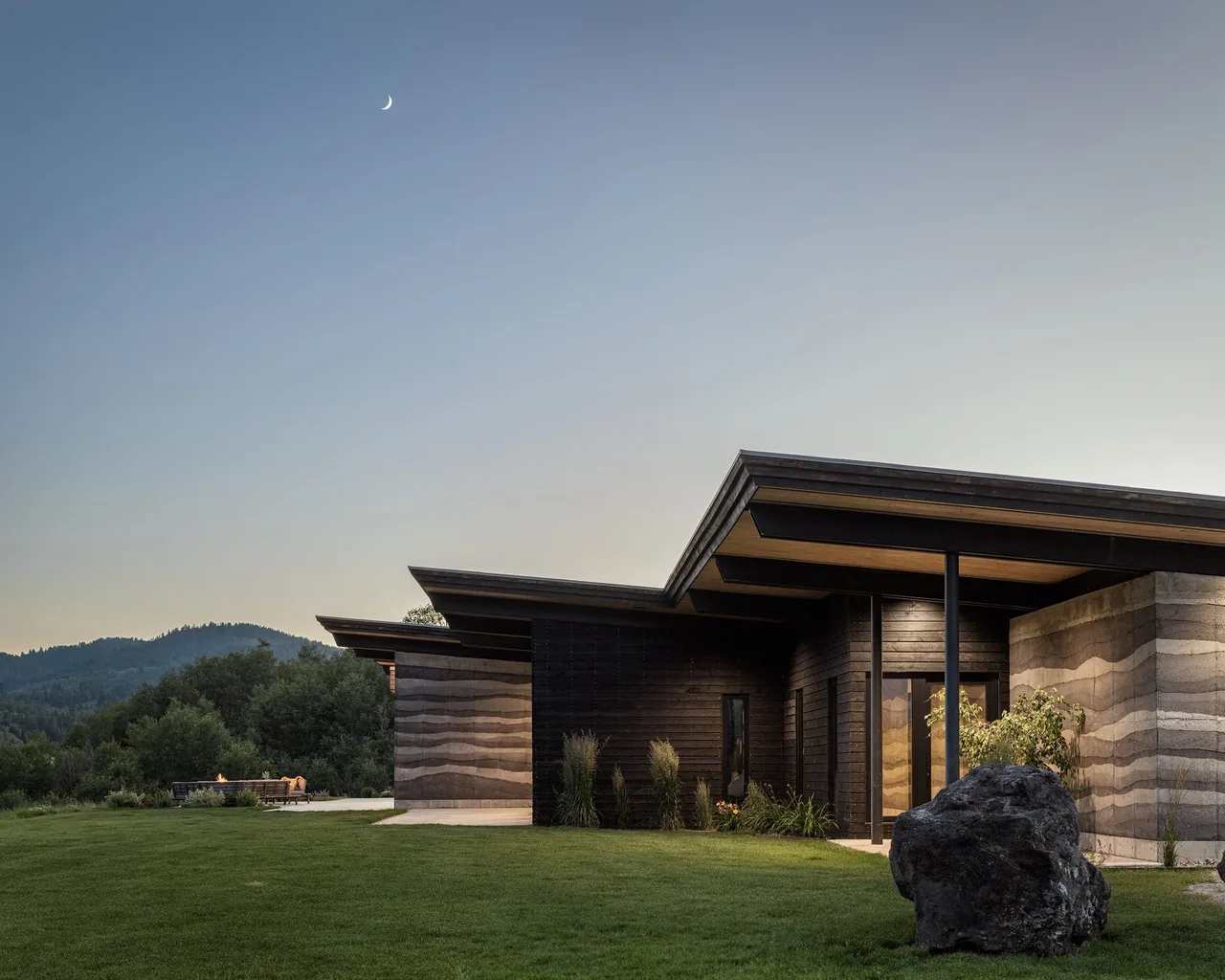 Exterior view of the Freedom Residence showing rammed earth and wood siding walls with flat roofs at dusk.