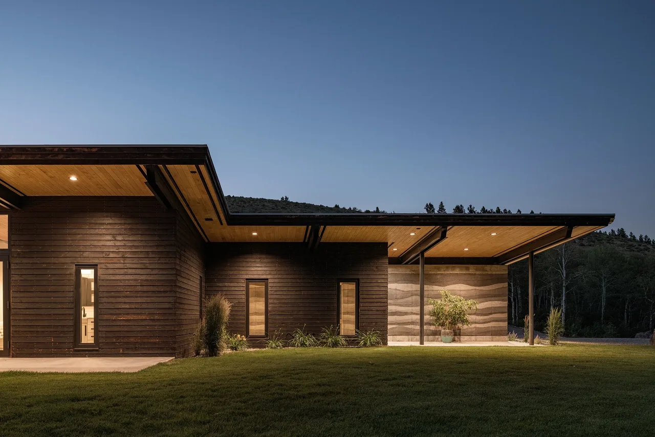 Evening view of the modern single-story Freedom Residence showing dark wood cladding and wood soffits under an extended flat roof.