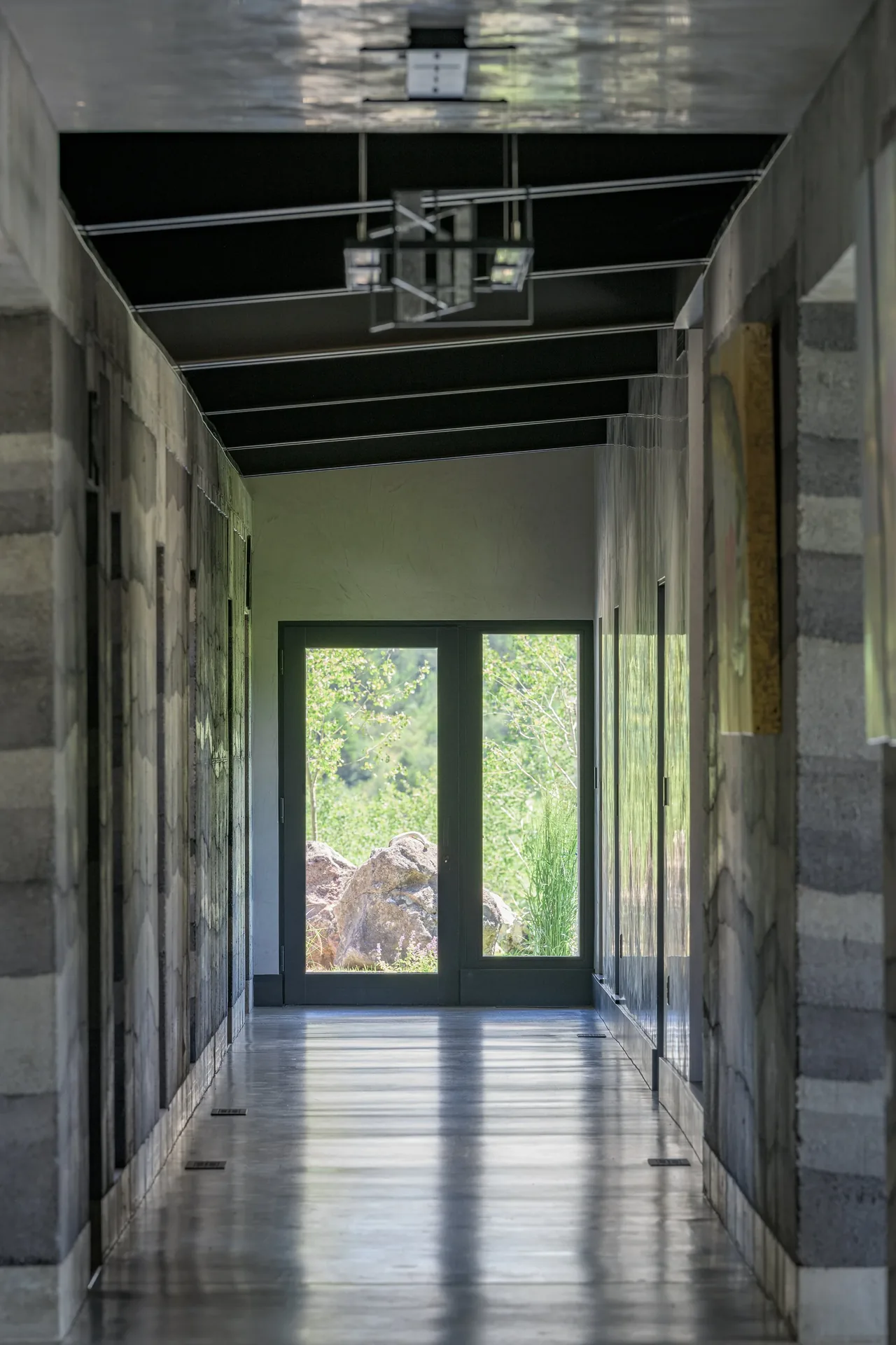 Interior hallway with polished concrete flooring and black ceiling leading to glass doors showing outdoor rocks and greenery