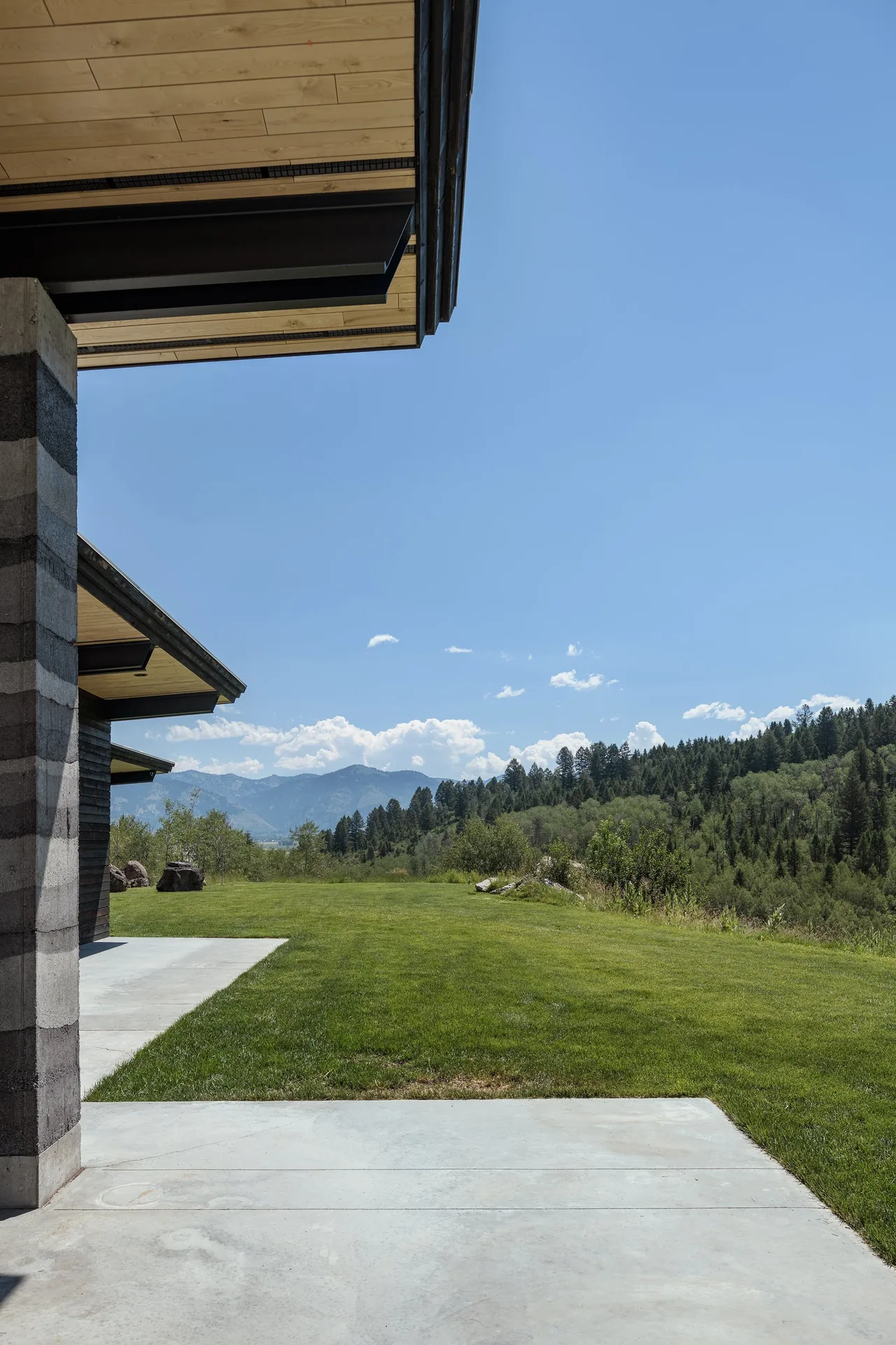 Partial exterior view of the Freedom Residence with concrete patio, wood-paneled overhangs, and surrounding landscape.