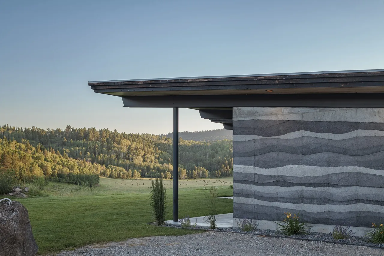 Side exterior view of a house with a layered concrete wall and an extended roof eave.