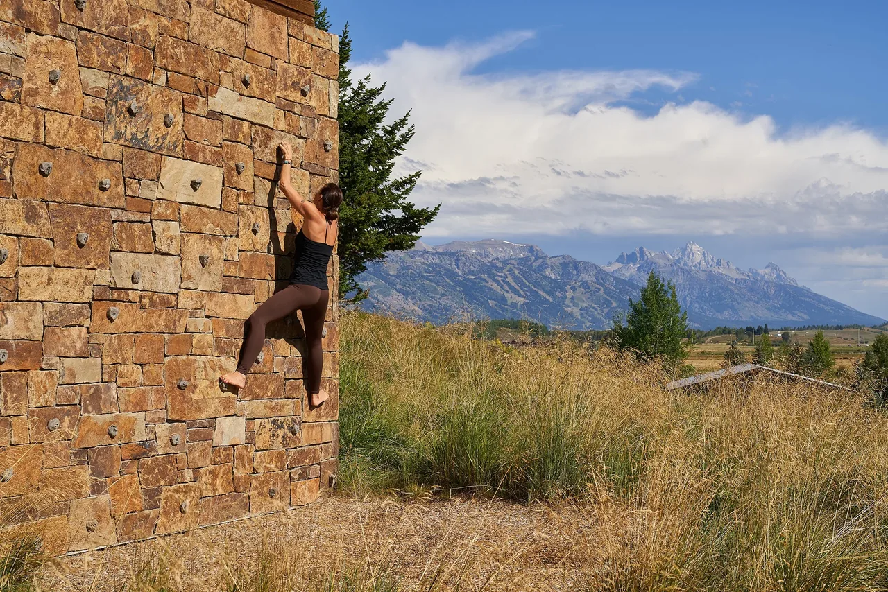 Outdoor climbing wall with stone facade and mountain landscape in the distance at Skyline Ranch Residence.