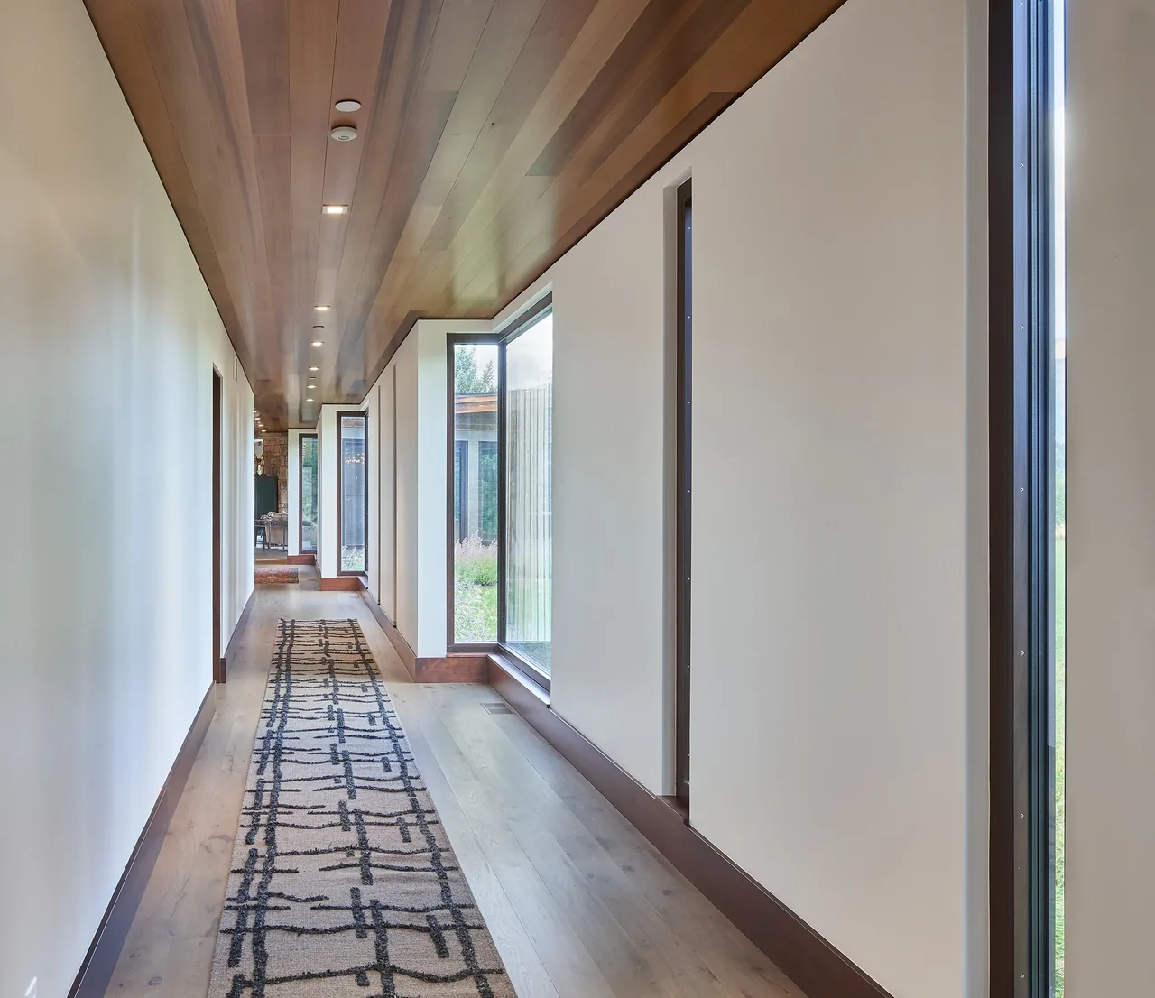 Interior hallway featuring wood ceiling, patterned runner rug, and floor-to-ceiling windows with black frames.