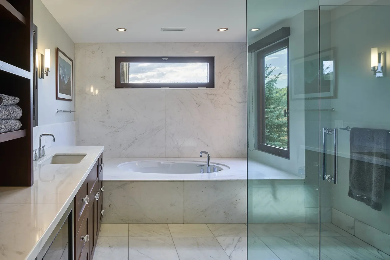 Skyline Ranch Residence bathroom features a marble bathtub and wall paneling with a glass shower enclosure.
