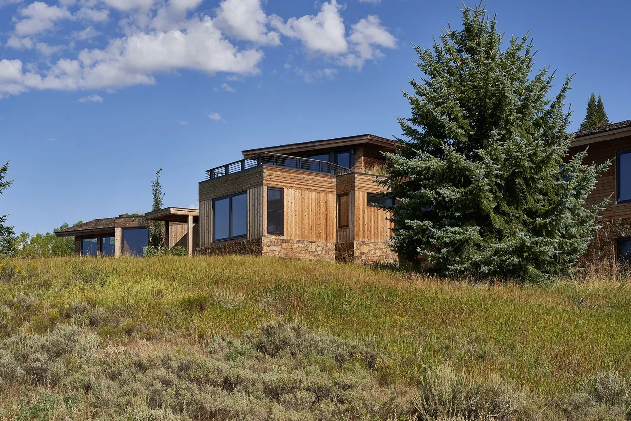 Skyline Ranch Residence features wood siding and stone base exterior, set against a natural grassy landscape.