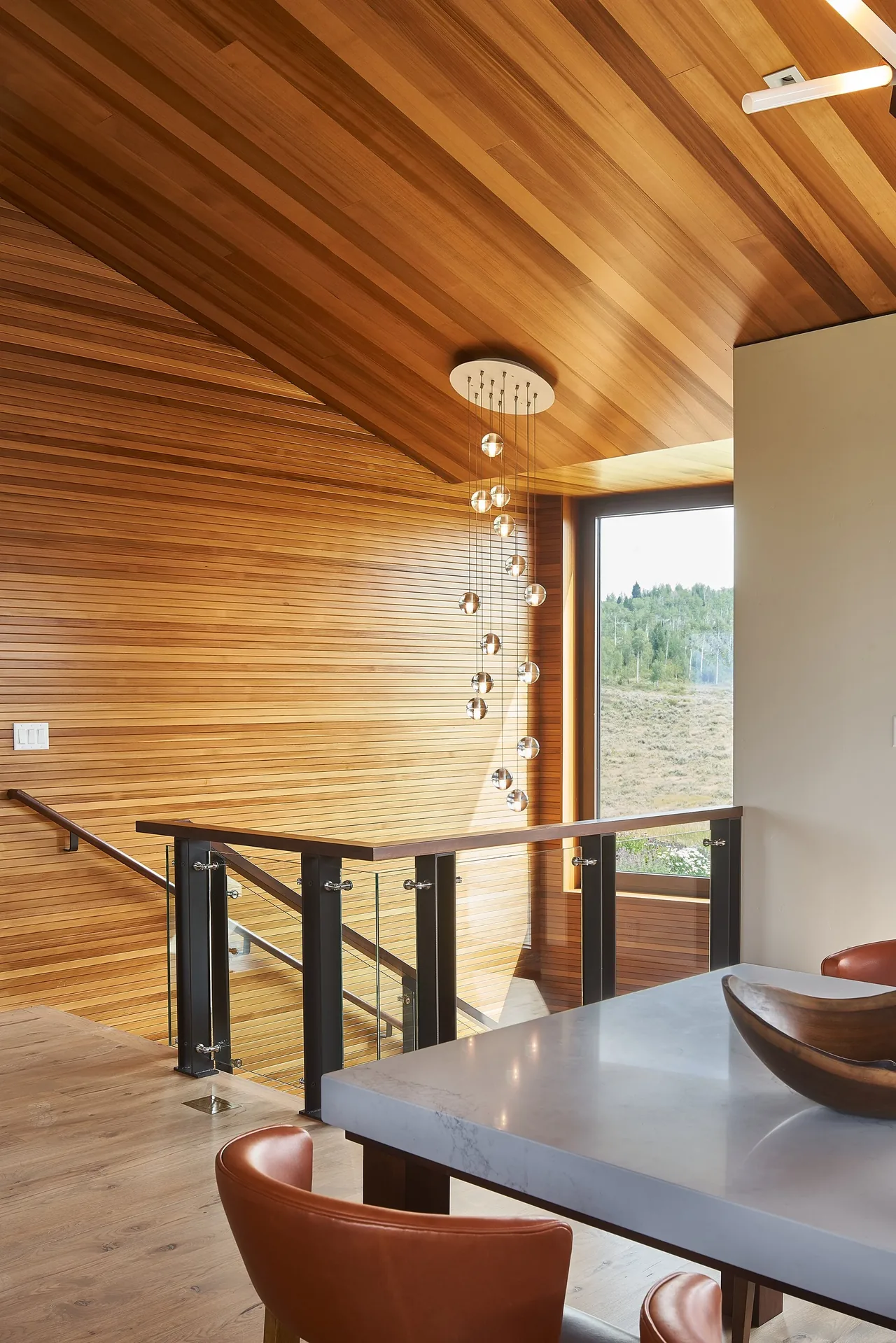 The stair landing features wood slat walls and ceiling with a glass balustrade and contemporary hanging glass orb lights.