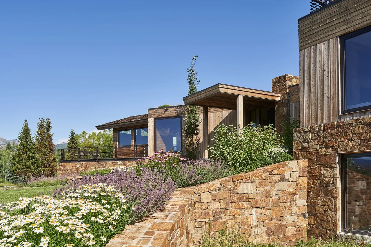 Skyline Ranch Residence features natural stone and wood siding with flat roof forms and expansive windows.