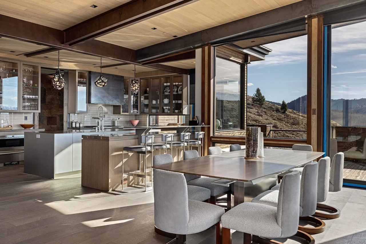 Open dining and kitchen space with floor-to-ceiling glazing and exposed steel beams.