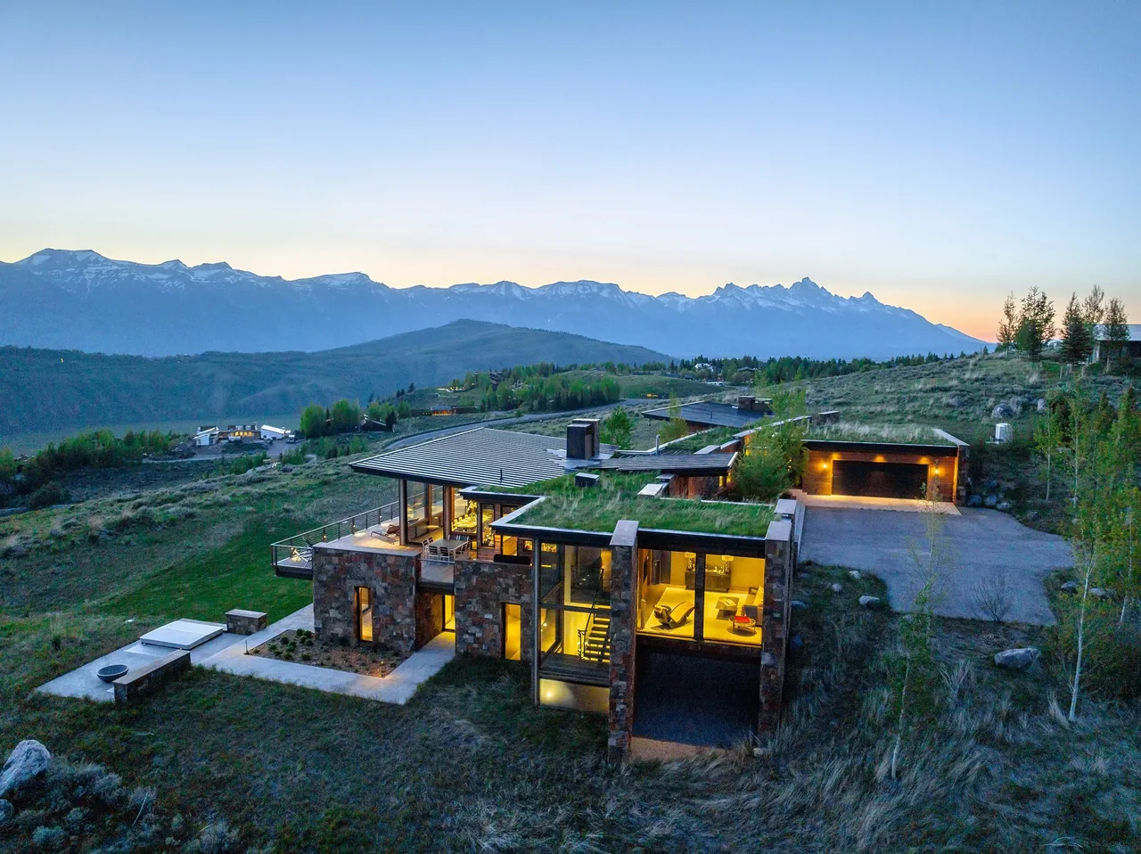 Ridge 52 Residence showcasing stone and glass exterior with green roofs on a hillside at dusk.