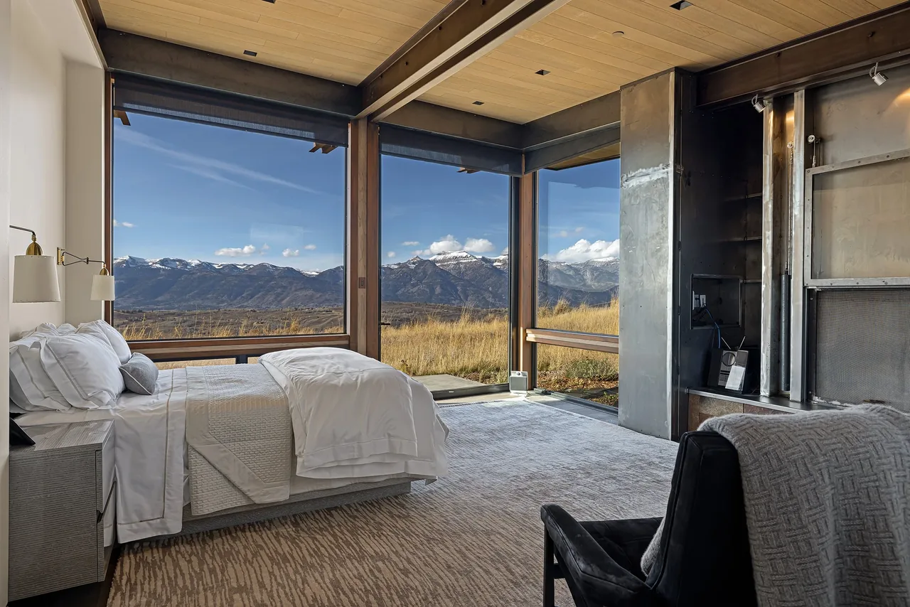 Bedroom featuring floor-to-ceiling corner windows with views of mountains and an adjacent lounge chair.